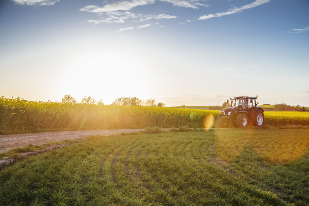 Tractor on dirt road amidst field during sunset